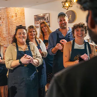 Group of people wearing aprons squeeze stroopwafel dough in their hands during a cooking class.