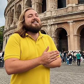 Person wearing yellow shirt smiling in front of the Roman Colosseum with their hands pressed together.