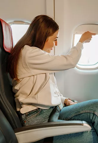 Person sits in the a window seat of a plane and lifts the window shade.