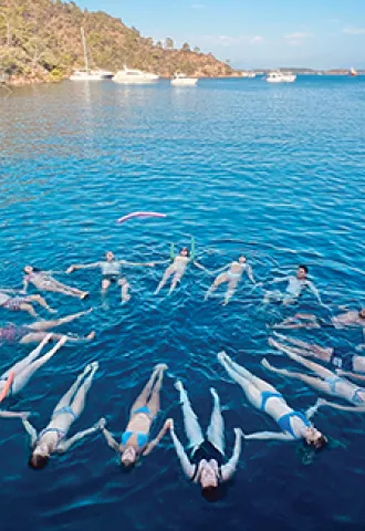 A group of people float together on the surface of the ocean, forming a star like shape.
