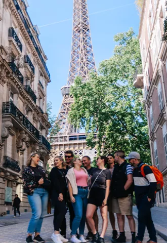 Group of people standing together on the street with the top of the Effiel Tower visible in the background.