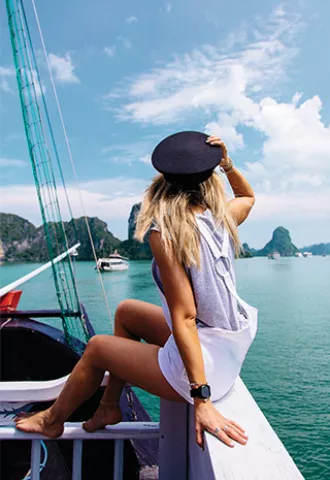 Person sitting on the edge of a sail boat while looking out at the ocean.