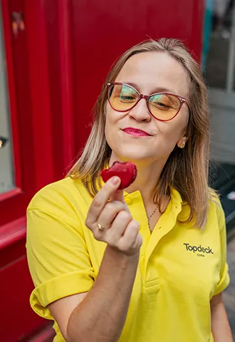 Topdeck trip leader in a yellow uniform holds a red macaroon in Paris.