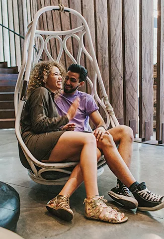 Two people sit together smiling in an egg shaped chair.