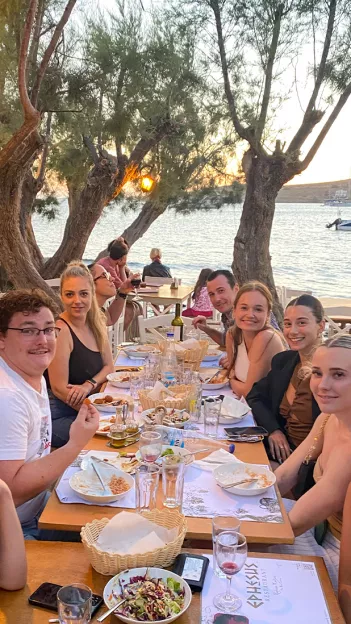 Group of people sitting at long table having a meal in Paros, Greece.