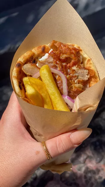 Hand holding a chicken gyro with potato fries inside.