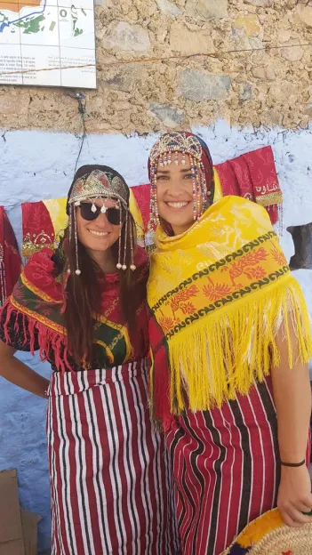 Two women smiling wearing long striped skirts and cheches with beaded detailing in Morocco.