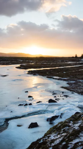  Frozen river in Iceland with sun setting on horizon.