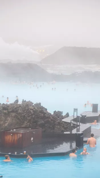 People soaking in the water of the Blue Lagoon geothermal spa in Iceland. The air is filled with steam from the pool.