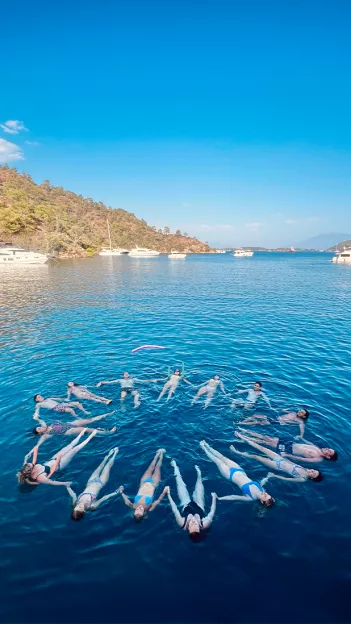 People floating on the surface of the ocean while holding hands in a star formation.
