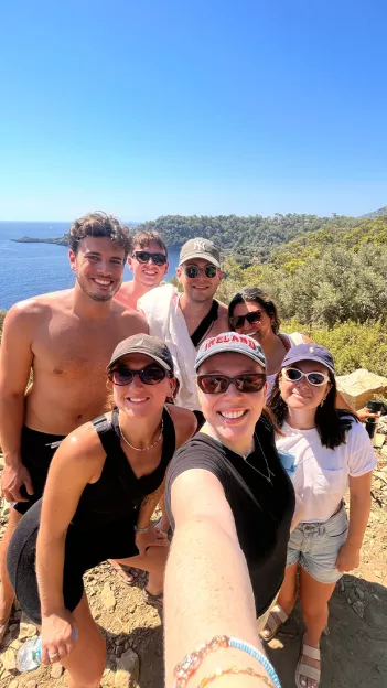 Seven people smile for a selfie style photo wearing activewear and swimwear.