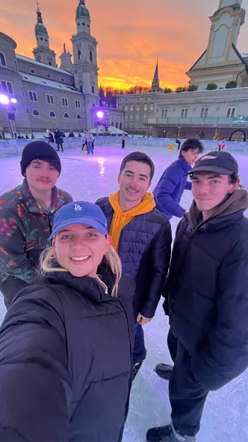 Four Topdeck travelers taking a selfie together while Ice Skating in front of Salzburg Cathedral in Austria.