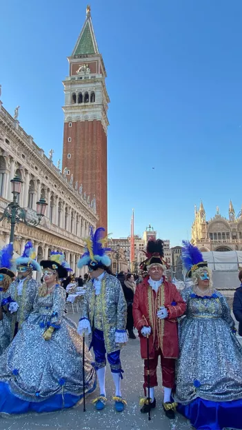 People wearing fancy costumes and masks with feathers at the Carnival of Venice.