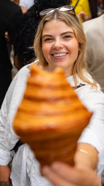 Person wearing sunglasses holds out a fresh croissiant that is out of focus.
