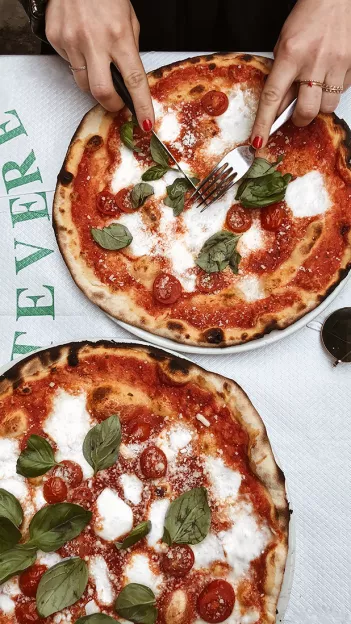 Person cuts into a margherita pizza with fresh basil.