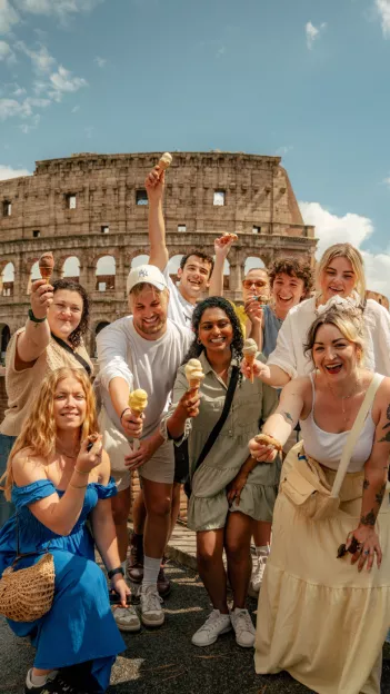 Group of people smiling while holding gelato and canolis in front of the colosseum in Rome.