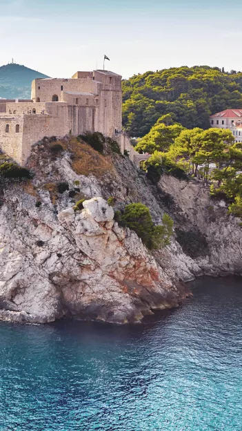 Stone building known as Fort Lovrijenac in Dubrovnik sitting on the edge of a cliff with water below.