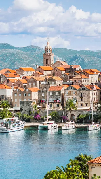 Sail boats float along the habour of Korčula, Croatia with the stone built city in behind.