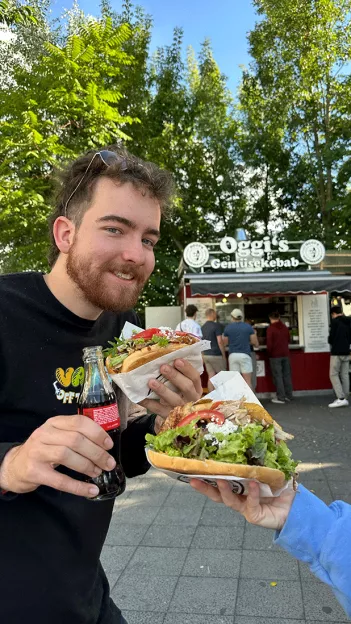 Man smiles while holding a bottle of soda and a doner kebab Berlin.