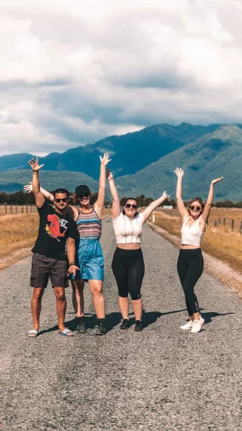 Four people stand on quiet road smiling with their hands in the air in New Zealand’s South Island.