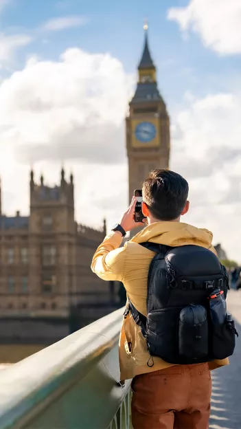 Person wearing a yellow jacket taking a photo on their phone of Big Ben in London.