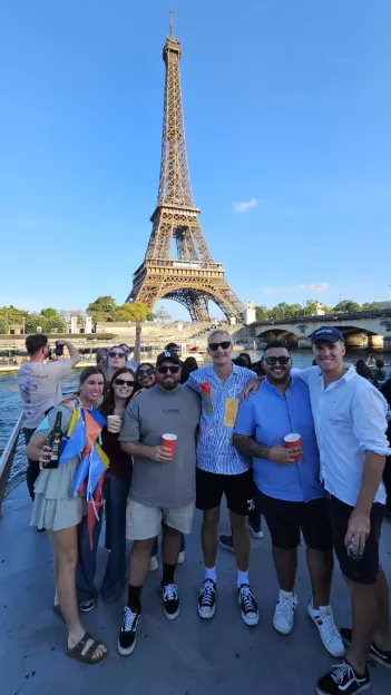 Group of people holding red cups posing together in front of the Eiffel Tower in Paris.