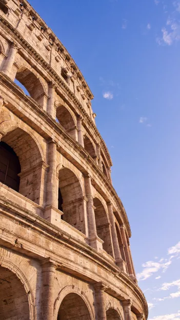 Side of Roman Colosseum featuring multiple archways made from stone.