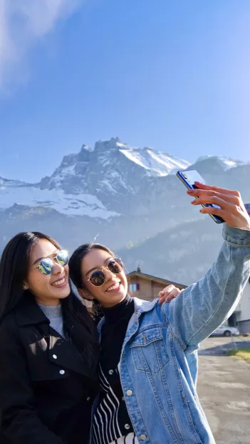 Two girls smiling while taking a selfie in front of the Swiss Alps.