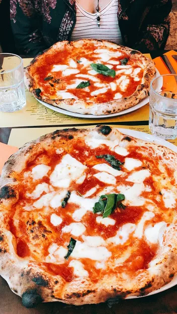  Two margarita pizzas with mozzarella and fresh basil sit on a table.