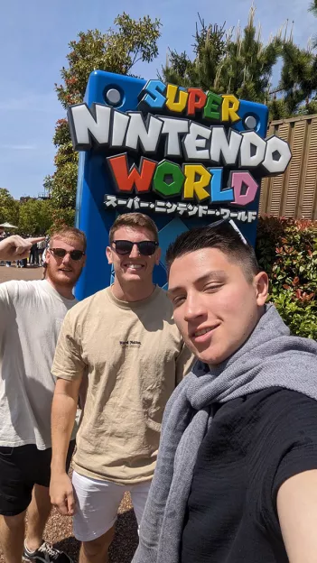 Three people smile together in front of the Super Nintendo World sign in Japan.