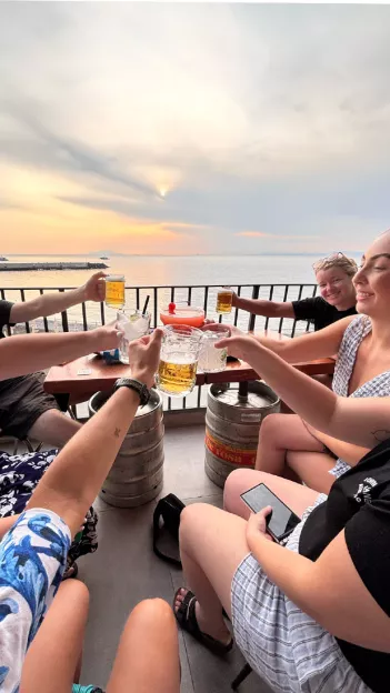 People sitting together raising a glass in a social gesture with the ocean behind them.