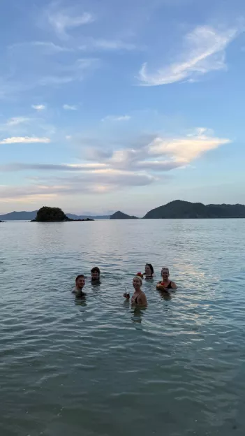 5 people smile while floating in the ocean with a few islands in the distance behind them.