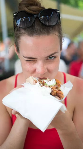 Person winks while biting into kebab style street food.