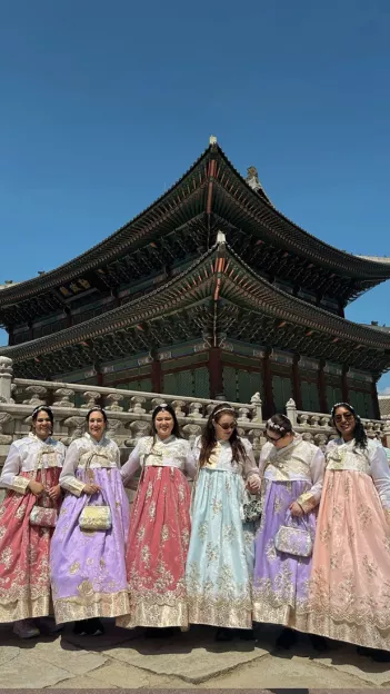  Six woman smile in traditional Korean dresses in front of Gyeongbokgung Palace in Seoul.
