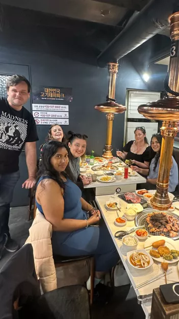 Small group of people at a Korean BBQ restaurant with copper coloured vents hanging above the table.