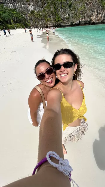 Two people take selfie together on white sand beach in Thailand.