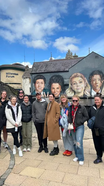 Group posing in front of the Derry Girls mural in Derry, Northern Ireland.