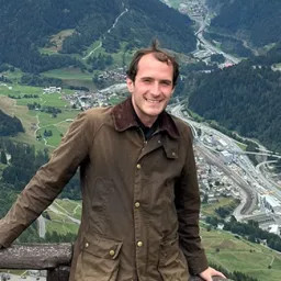 Person smiling with the view over a green valley behind them.