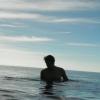 man standing submerged in the sea. His outline is a silhouette.