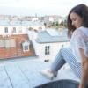 Woman sitting on a roof wearing a white top and blue-and-white striped trousers