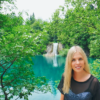 Smiling, blonde woman standing in green scenery 