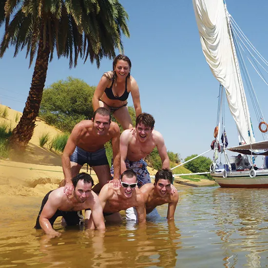 Six people making a human pryamid stack on the edge of the river in their swimsuits.