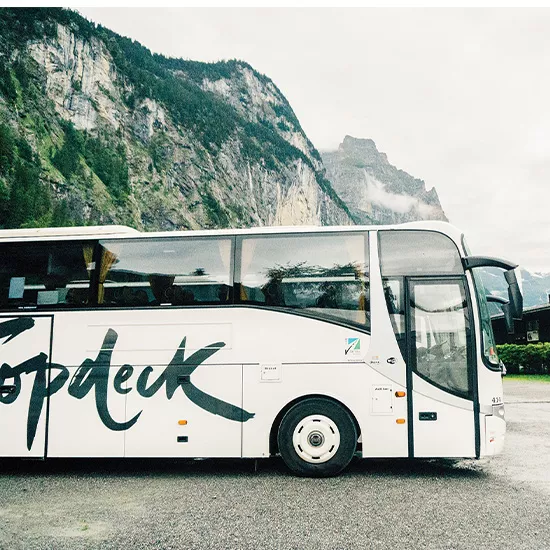 A Topdeck tour bus parked, with a view of the Swiss Alps behind it.