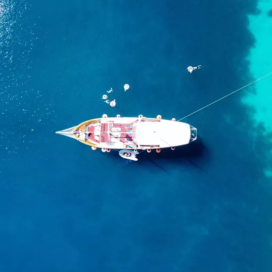 Birds eye view of sail boat in the blue waters of Greece. People float in the water near the boat.
