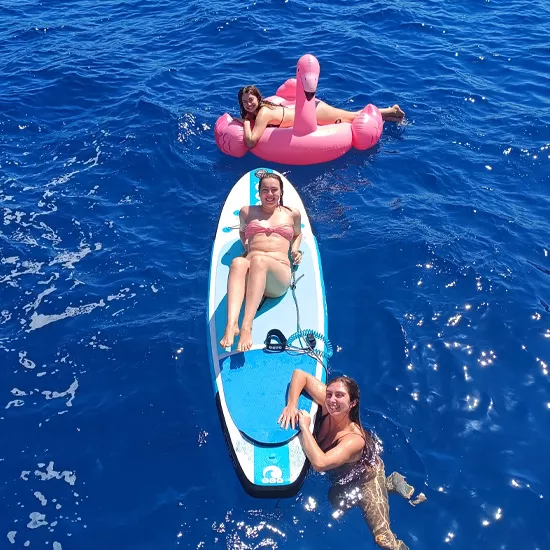 Person floats on inflatable flamingo near a person laying on a paddle board with someone else floating nearby.