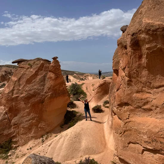 Person standing with their hands in the air. They stand on a dirt road between two rock formations in Cappadocia.