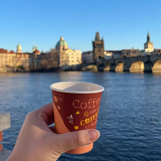A Topdeck traveler enjoying a cup of coffee and a view of the the city of Prague and one of it's iconic bridges.