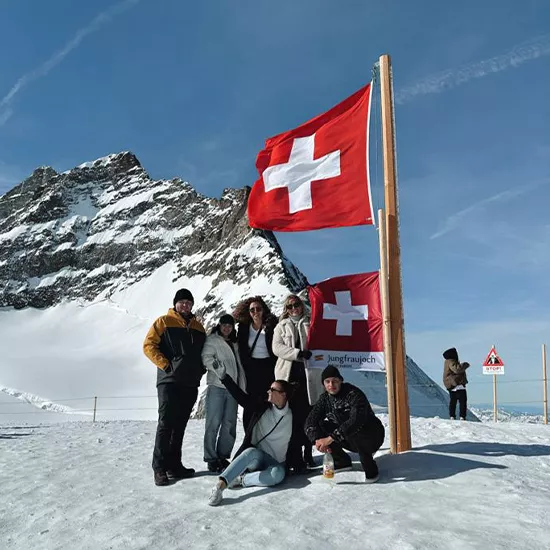 Topdeck travelers posing with a Swiss flag atop the Swiss Alps.