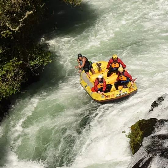 Four people in helmets sit inside a yellow raft on the downward slope of small rapid in Kaituna River.