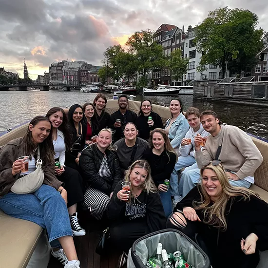 Group of people smiling together at the front of a canal boat in Amsterdam.